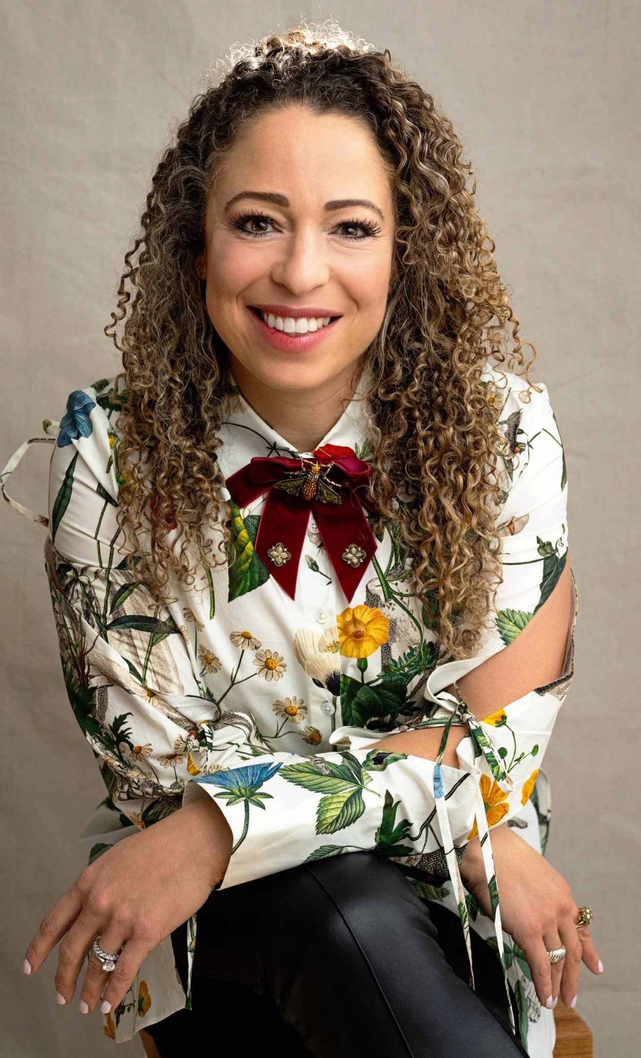 Woman wearing a floral blouse with a red bow tie against a plain background